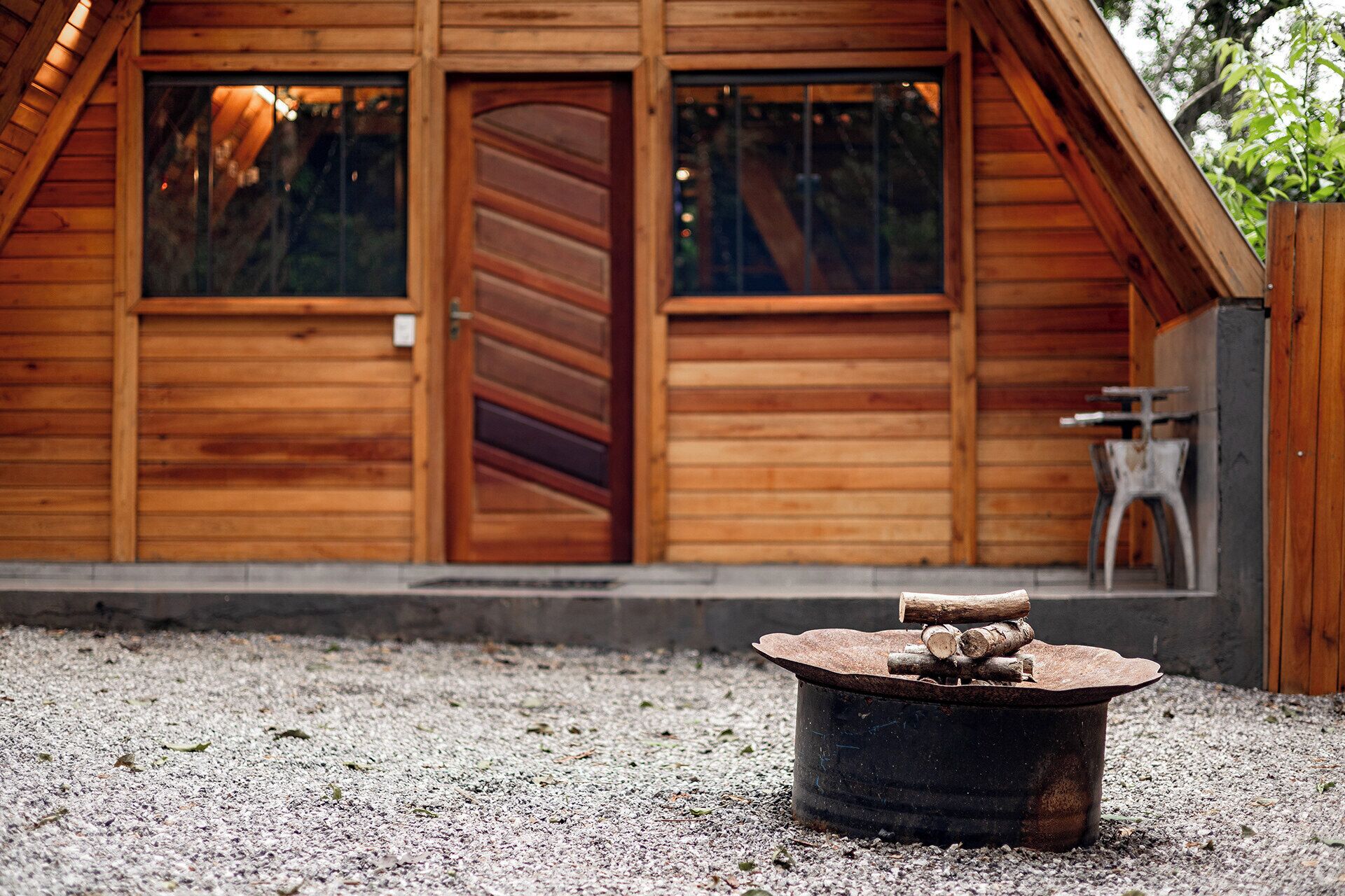 A wooden cabin with a large sliding door, a small table, and a fire pit in the foreground.