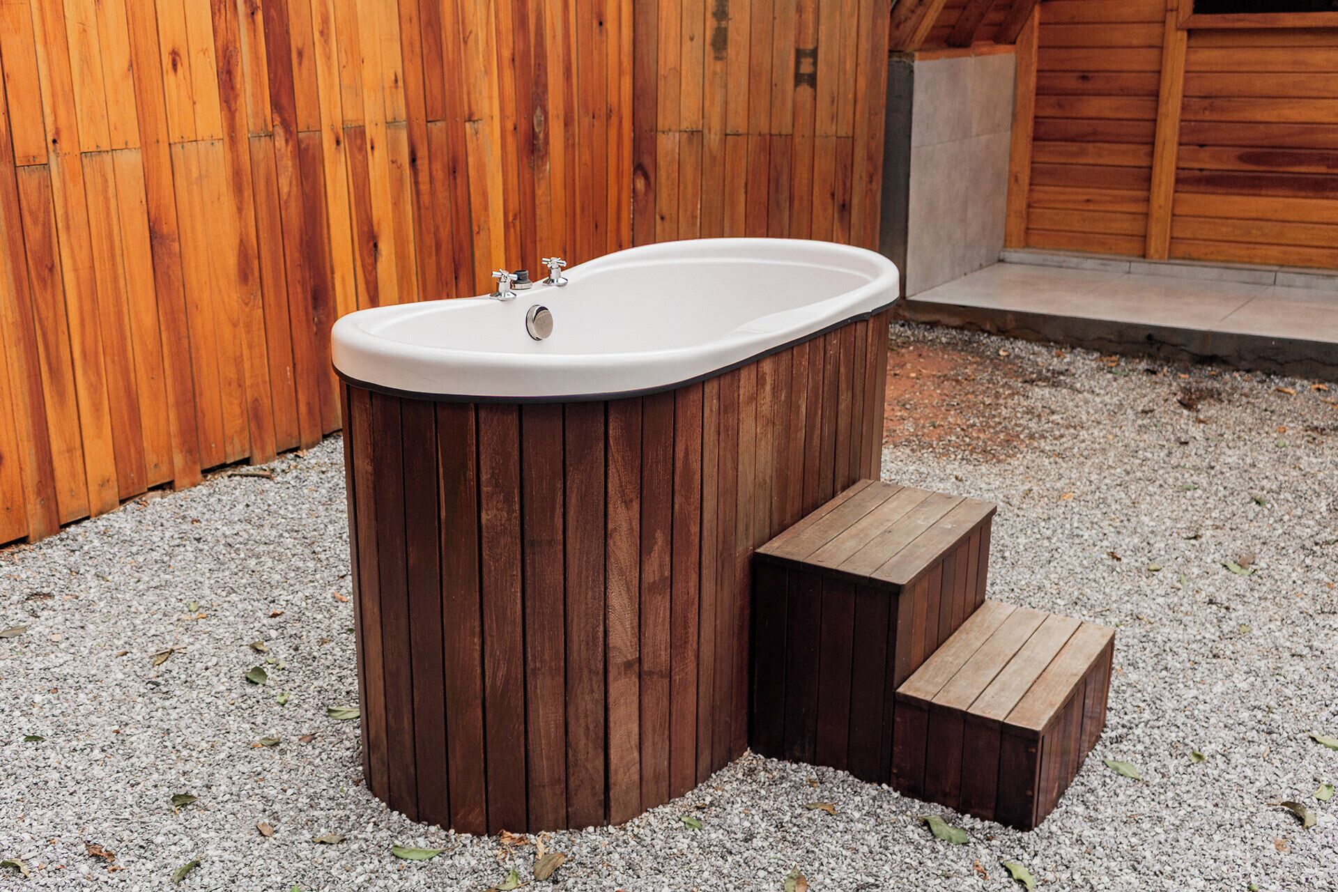 A wooden hot tub with a white interior, surrounded by gravel and wooden steps.