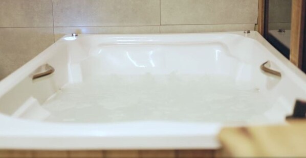Una bañera blanca con detalle de madera, frente a una pared de azulejos.