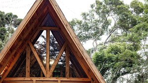 A wooden cabin with a triangular roof, large windows, and a fire pit in the foreground. - CHALÉS SUIÇOS - Românticos na Natureza para Adultos (Itapecerica da Serra)