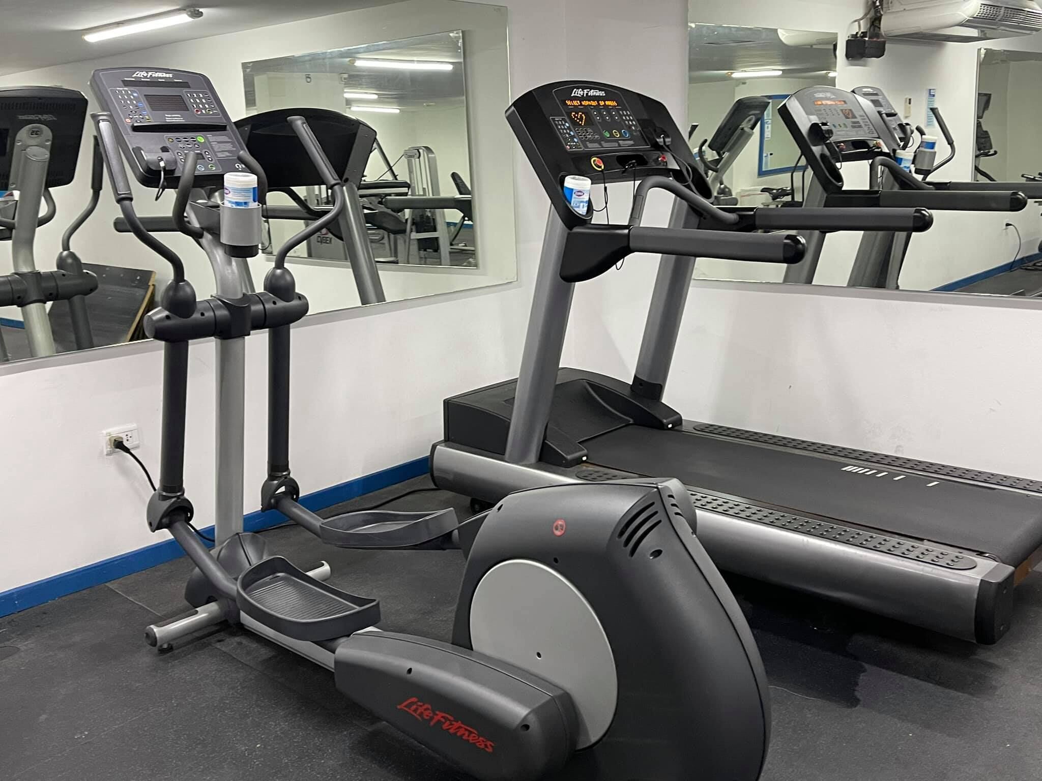 A gym with cardio machines, including treadmills and an elliptical, and a mirrored wall.
