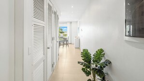A hallway with white walls, a tiled floor, and a potted plant. There is a door with louvered shutters and a window with blinds. - Azure Heaven, Breathtaking views, Pool, Gym (Maho)
