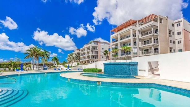 A swimming pool with a clear blue water, surrounded by lounge chairs and palm trees. - Azure Heaven, Breathtaking views, Pool, Gym (Maho)