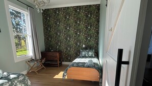 Ett sovrum med två sängar, ett trägolv, en kristallkrona, ett fönster med gardiner och en vägg med ett blommönster.