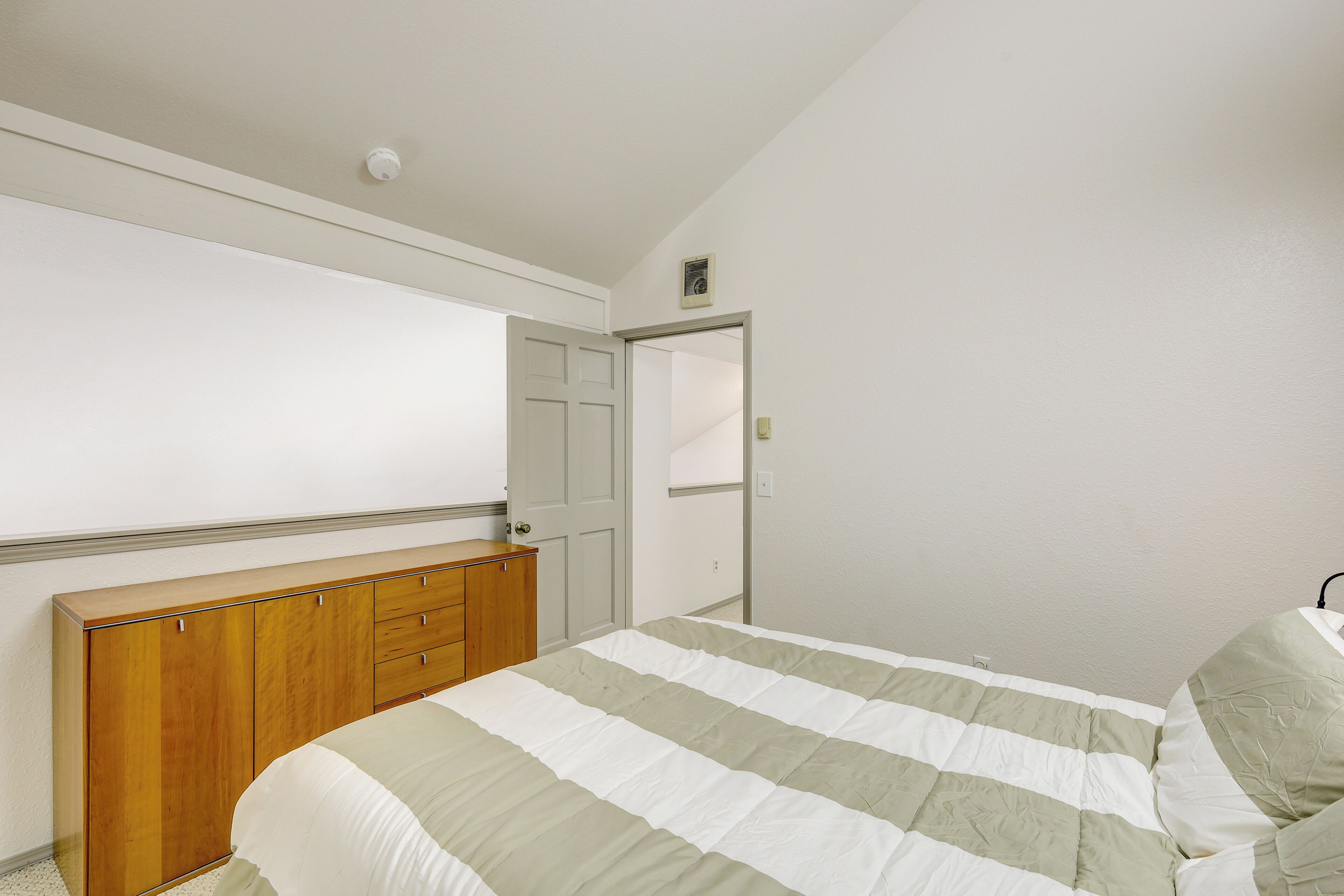 A bedroom with a bed, wooden dresser, and a door leading to another room.