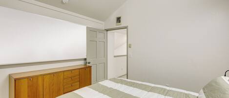 A bedroom with a bed, wooden dresser, and a door leading to another room.