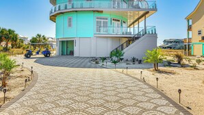 A multi-story building with a curved facade, a central staircase, and a paved entrance area with palm trees. - Golf Cart + Elevator: Retreat 1 Block to Beach (Pensacola Beach)