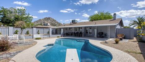A swimming pool with a patio area, a covered outdoor seating area, and a mountain in the background.