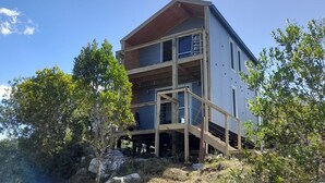 A modern multi-story building with a wooden deck and glass balconies, surrounded by trees and rocks.