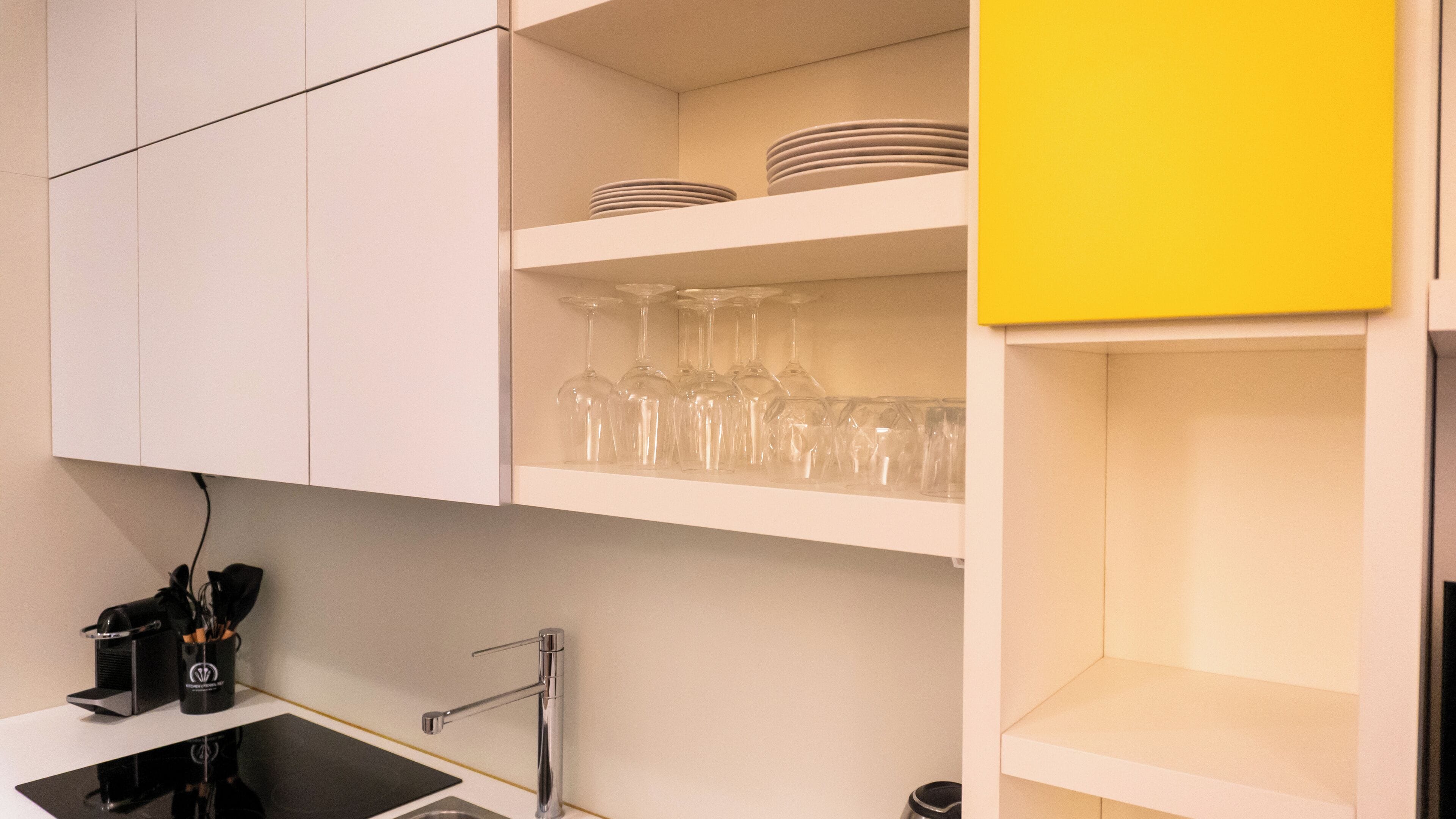 A modern kitchen with white cabinets, a yellow accent wall, and a stainless steel sink.