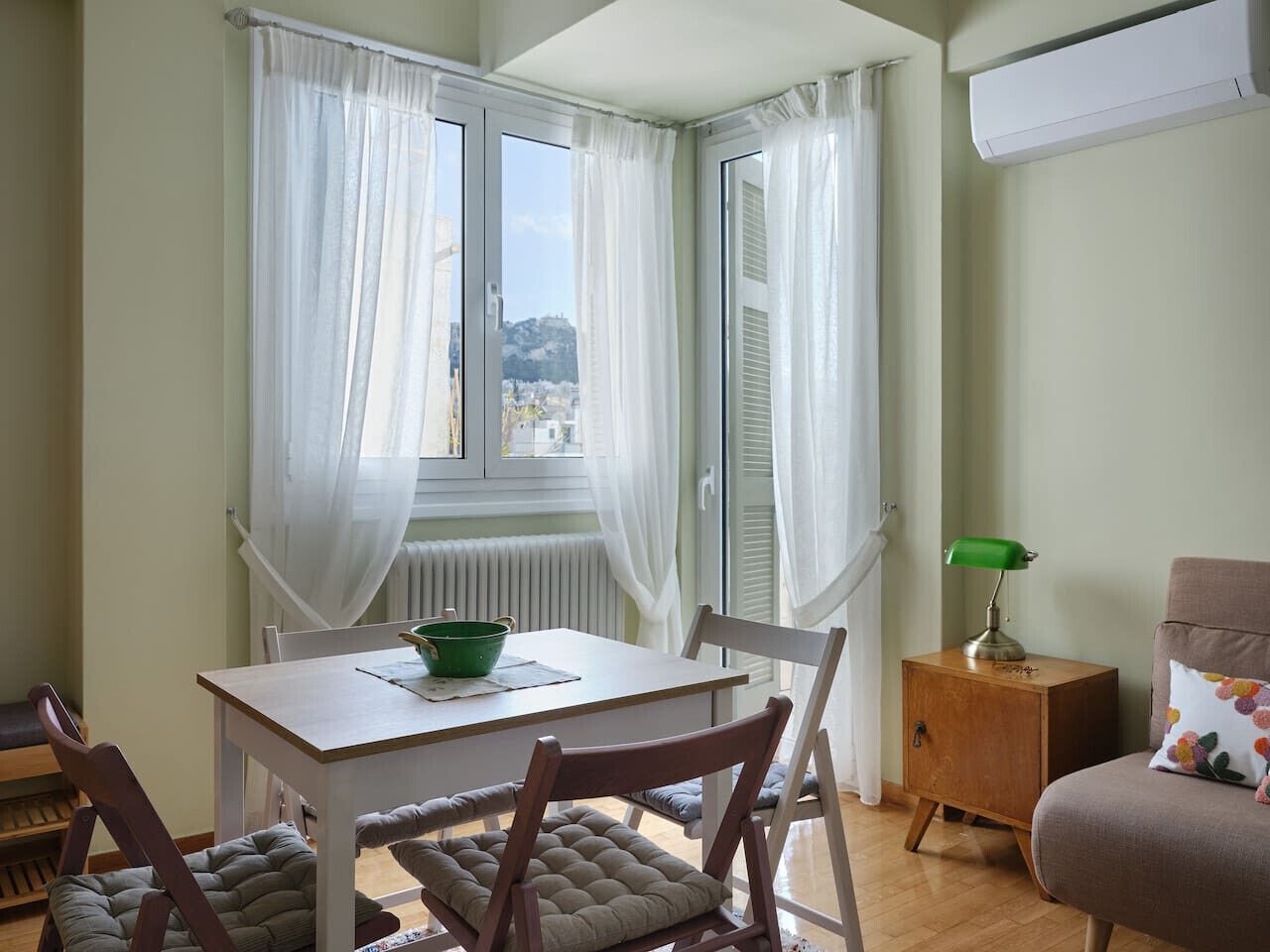 Una habitación con una mesa de comedor, sillas, un armario pequeño y una ventana con cortinas.