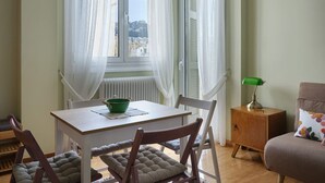 A room with a dining table, chairs, a small cabinet, and a window with curtains.