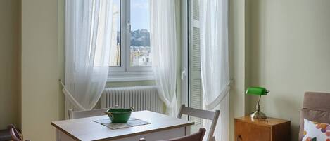 Una habitación con una mesa de comedor, sillas, un armario pequeño y una ventana con cortinas.