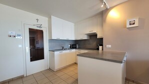 Ett modernt kök med vita skåp, en grå bänkskiva och en inbyggd mikrovågsugn.