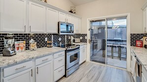 A modern kitchen with white cabinets, a black and white backsplash, a microwave, a stove, and a glass door leading to a balcony. - 5BR Hideaway w/ Heated Pool/Hot Tub/Billiards Table (Glendale)