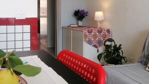 Ein Essbereich mit Tisch, Stühlen, einem an der Wand befestigten Schiffsrad, einem gerahmten Gemälde, einem kleinen Tisch mit Lampe und einem Blumentopf.