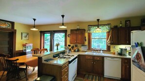 Une cuisine avec des meubles de rangement en bois, une cuisinière à gaz, un évier et un coin repas avec des chaises.