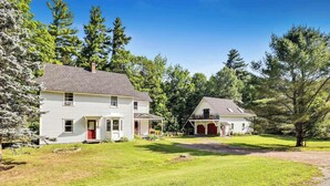 Une maison à deux étages avec une porte rouge et un garage, entourée d’une pelouse bien entretenue et d’arbres.