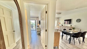 A hallway with a wooden floor, white walls, and a dining area with a table and chairs.