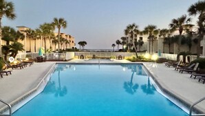 A swimming pool with lounge chairs and palm trees, surrounded by buildings.