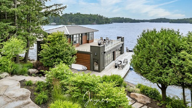 Una casa moderna con un balcón que da a un lago, rodeada de exuberante vegetación.
