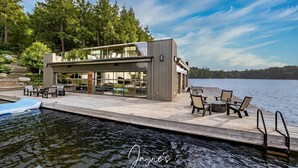 Una moderna casa flotante con terraza, asientos exteriores y una piscina.