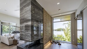 Una sala de estar moderna con chimenea de piedra, ventanas amplias y vistas a un lago.