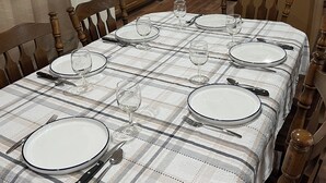 Un coin repas avec une table dressée pour six personnes, des chaises en bois et une cuisine en arrière-plan.