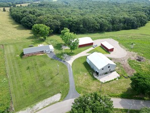 Vue aérienne d’une ferme avec des granges, une route sinueuse et des champs verdoyants environnants.