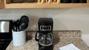 Une cuisine équipée d’une machine à café, d’ustensiles et de différents plats rangés sur des étagères.