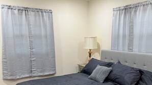 Une chambre à coucher avec un lit, des rideaux, une table de chevet, une lampe et un ventilateur de plafond.