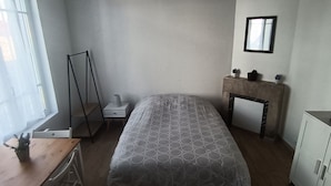 A bedroom with a bed, a bedside table, a nightstand, a dresser, a mirror, and a window with curtains.