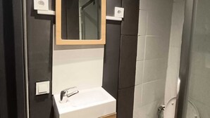 A modern bathroom with a white sink, a wooden vanity, a mirror, and a toilet.