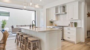 A modern kitchen with white cabinetry, a central island with stools, a stove, and pendant lighting. - Sunstone Retreat: Hot Tub + Desert Color Lagoon + Beaches, Hot Tub (St. George)