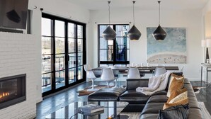 A modern living room with a fireplace, a glass coffee table, a black leather sofa, and a dining area with white chairs and a large window. - 121 Hotel Buyout by Avantstay Buyout of 121 Hotel w/ Living Areas & Meeting Room! Sleeps 58 (Nashville)