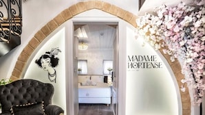 A luxurious bedroom with a large bed, a chandelier, and a black armchair. - Madame Hortense Hotel (Chania)