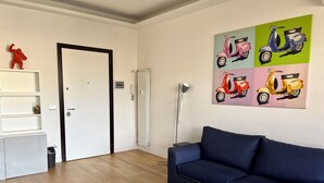 Un soggiorno moderno con un divano blu scuro, un tavolino da caffè bianco e un'opera d'arte raffigurante uno scooter colorato appesa al muro.