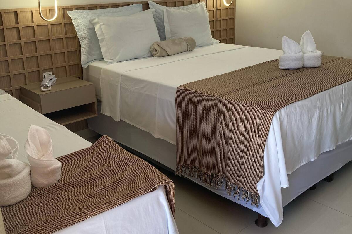 Une chambre d’hôtel avec deux lits, chacun étant équipé de draps blancs et de couvertures à rayures marron. Il y a deux tables de chevet avec des serviettes et un téléphone.