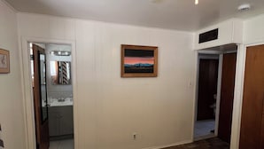 Un dormitorio con cama, ventilador de techo, un cuadro y un baño visible a través de una puerta abierta.