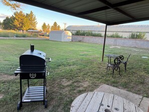 Un jardin avec un barbecue, une table et des chaises, le tout installé sous une zone abritée.