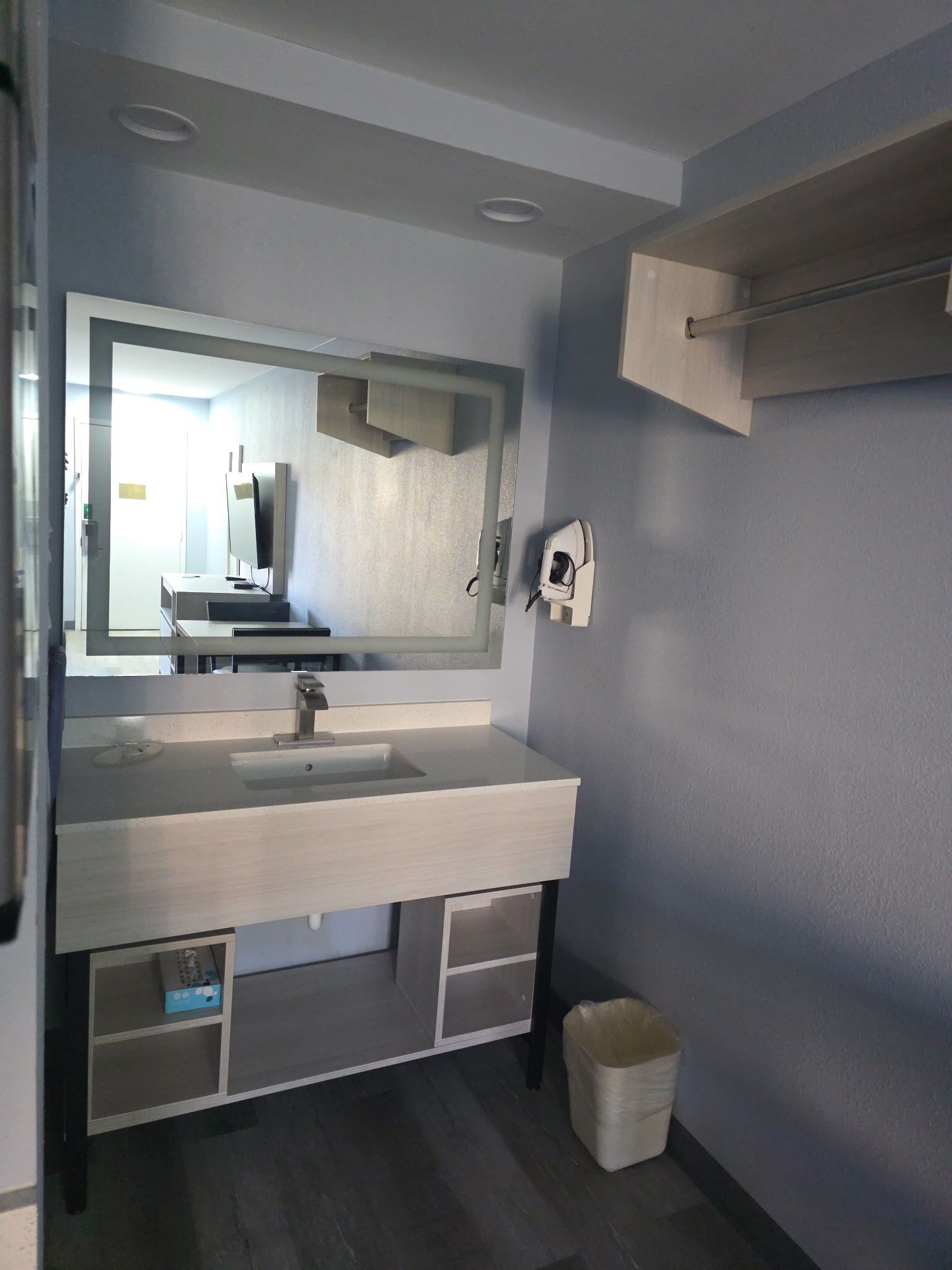 A modern bathroom with a large mirror, a sink, and a trash bin.