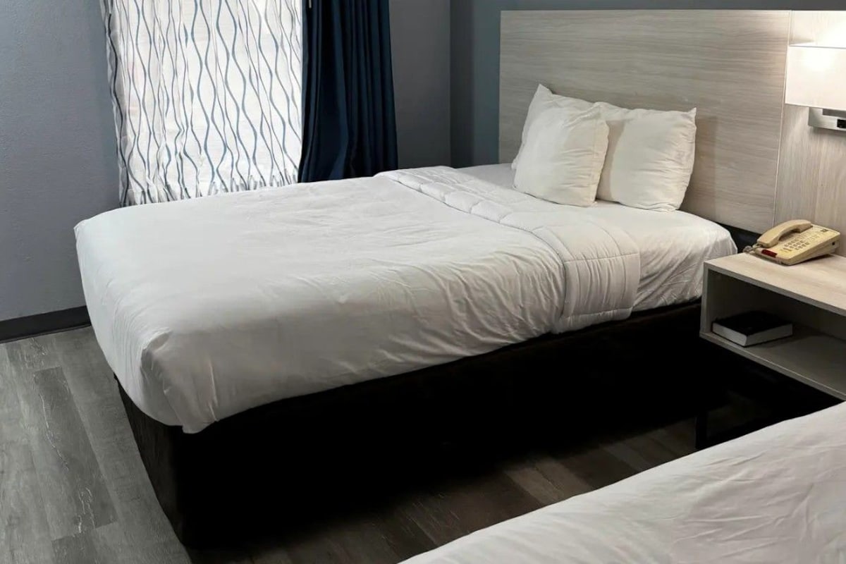 Una habitación de hotel con una cama, una mesita de noche con teléfono y una cortina estampada.