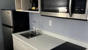 Una cucina compatta con frigorifero in acciaio inox, forno a microonde, lavello e piano cottura a induzione.