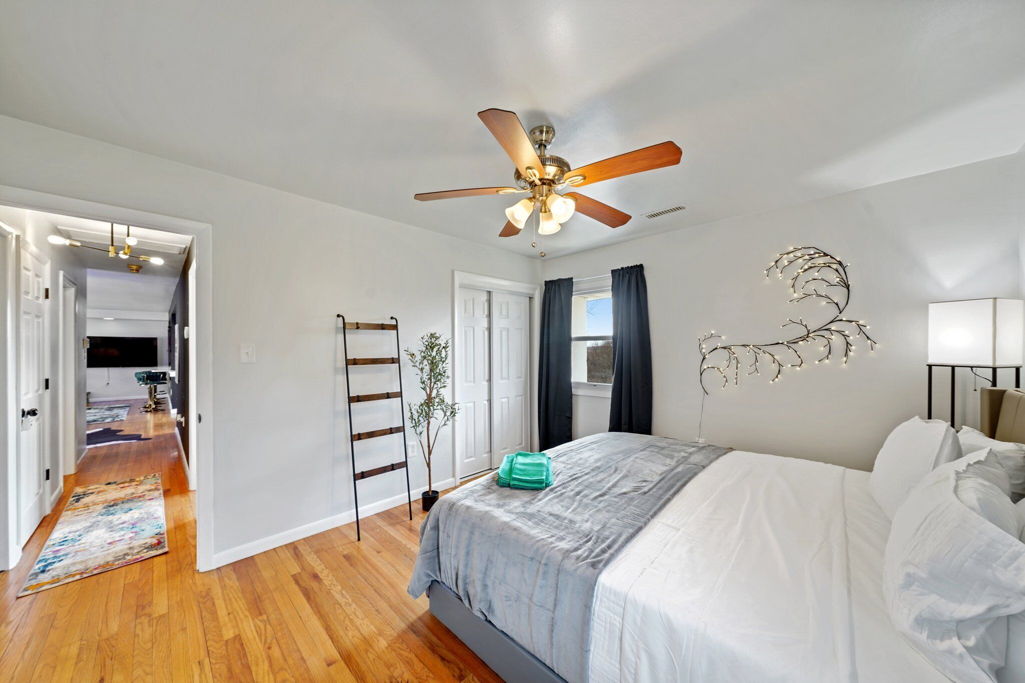 A bedroom with a bed, a ceiling fan, a wall-mounted light fixture, and a door leading to another room.