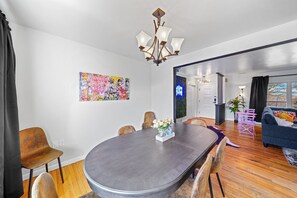 A dining area with a large table, chairs, and a chandelier. There is a colorful painting on the wall and a plant in the corner. - Comfort, Fun, & charming! - 5BR oasis w/ Pool (Coatesville)