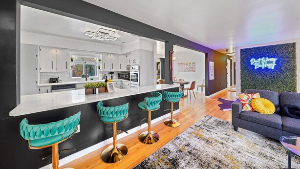 A modern kitchen with white cabinets, a black countertop, and three teal bar stools.
