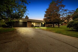 A residential house with a garage, driveway, and surrounding trees. - Comfort, Fun, & charming! - 5BR oasis w/ Pool (Coatesville)