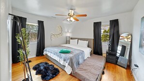 A bedroom with a bed, a ceiling fan, a dresser, a mirror, and a window with curtains.