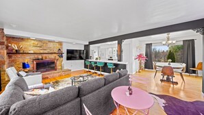 A modern living room with a stone fireplace, a grey sectional sofa, a pink round table, and a dining area with a white table and chairs.