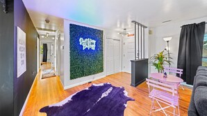 A modern living room with a wooden floor, a purple rug, a neon sign, and a small table with chairs.
